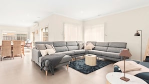 A modern living room with a grey sectional sofa, a round coffee table, and a dining area with a wooden table and chairs.