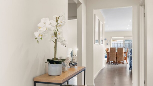 Un couloir agrémenté d’une orchidée en pot, une petite table ornée d’objets décoratifs et un coin repas avec des chaises et une table.