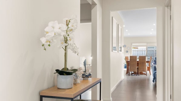 A hallway with a potted orchid, a small table with decorative items, and a dining area with chairs and a table.