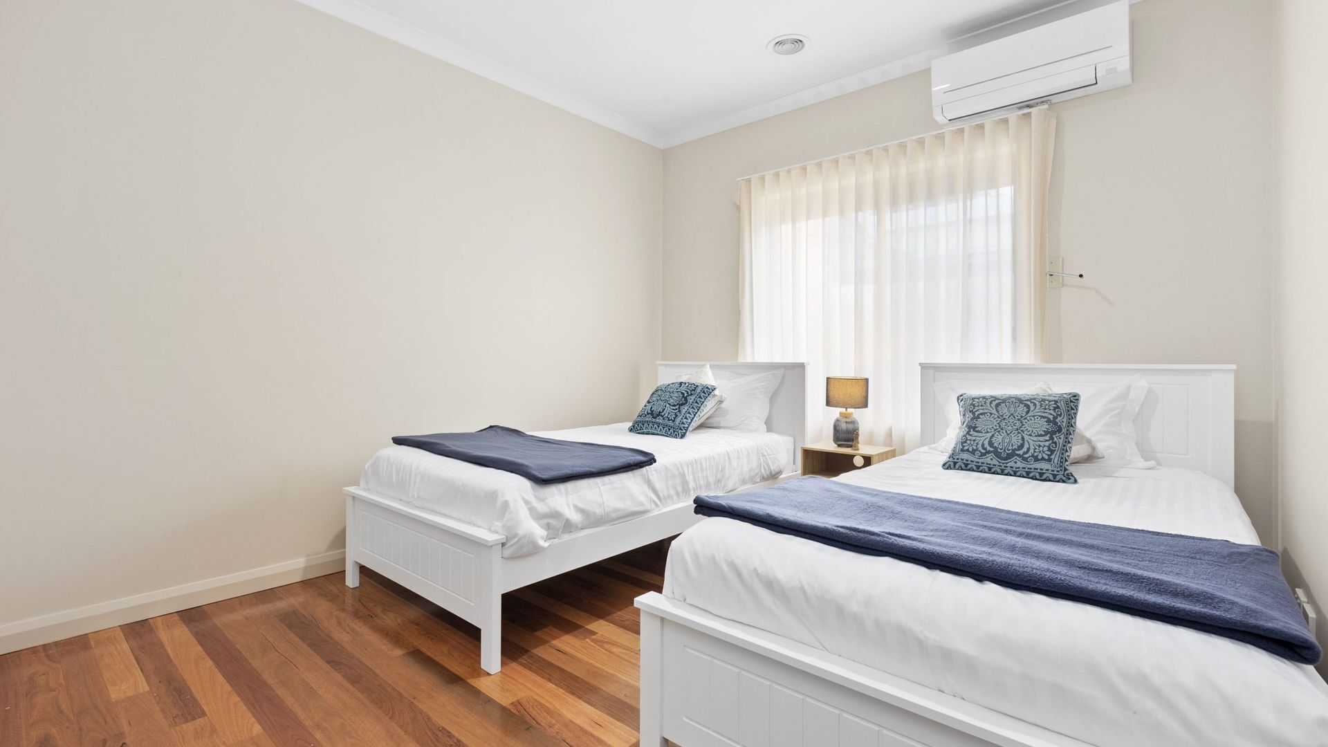 Ein Hotelzimmer mit zwei Betten, einem Vorhangfenster, einer Klimaanlage und Holzboden.