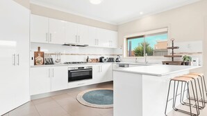 Une cuisine moderne avec des meubles blancs, une cuisinière à gaz, un four, un évier et une fenêtre donnant sur un immeuble et des arbres.