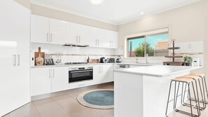 A modern kitchen with white cabinetry, a gas stove, an oven, a sink, and a window with a view of a building and trees.