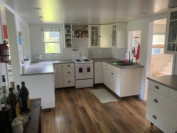 A compact kitchen with white cabinets, a stove, and a sink.
