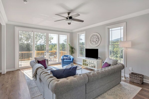A spacious living room with a grey sofa, a blue armchair, and a flat-screen TV on a white cabinet.