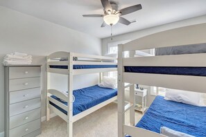 Une chambre avec un lit superposé, un ventilateur de plafond, une commode et une petite table de chevet.