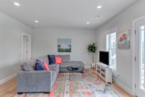 A living room with a grey sectional sofa, a flat-screen TV, a patterned rug, and artwork on the walls. - Clean family-friendly 5BR in the HEART of Virginia's Wine Country (Afton)