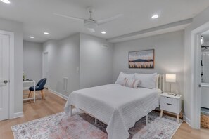 Een slaapkamer met een bed, nachtkastjes, een bureau, een stoel en een plafondventilator.