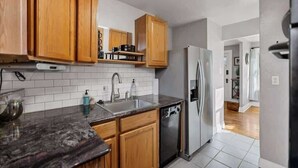 A modern kitchen with wooden cabinets, a stainless steel refrigerator, and a granite countertop. - Casa Mosaic! Downtown w BBQ & Workspace! (Colorado Springs)