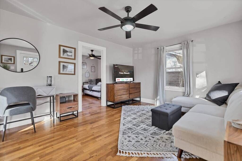 A modern living room with a ceiling fan, a TV, a sofa, a chair, and a wooden cabinet.