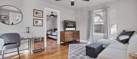Una sala de estar moderna con ventilador de techo, televisor, sofá, sillón y mueble de madera.