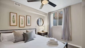 A hotel room with a bed, a ceiling fan, a window with curtains, and framed botanical prints on the wall. - Casa Mosaic! Downtown w BBQ & Workspace! (Colorado Springs)