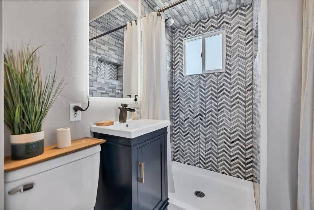 A modern bathroom with a black and white chevron-patterned shower curtain, a white sink with a wooden countertop, and a potted plant.