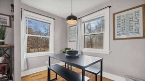 A dining area with a table and bench, large windows, and a hanging light fixture. - Casa Mosaic! Downtown w BBQ & Workspace! (Colorado Springs)
