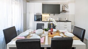 A modern kitchen with white cabinets, a built-in oven, and a large flat-screen TV.