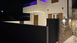 Une maison moderne à deux étages, dotée d’un balcon, d’un mur en pierre et d’une porte en bois.
