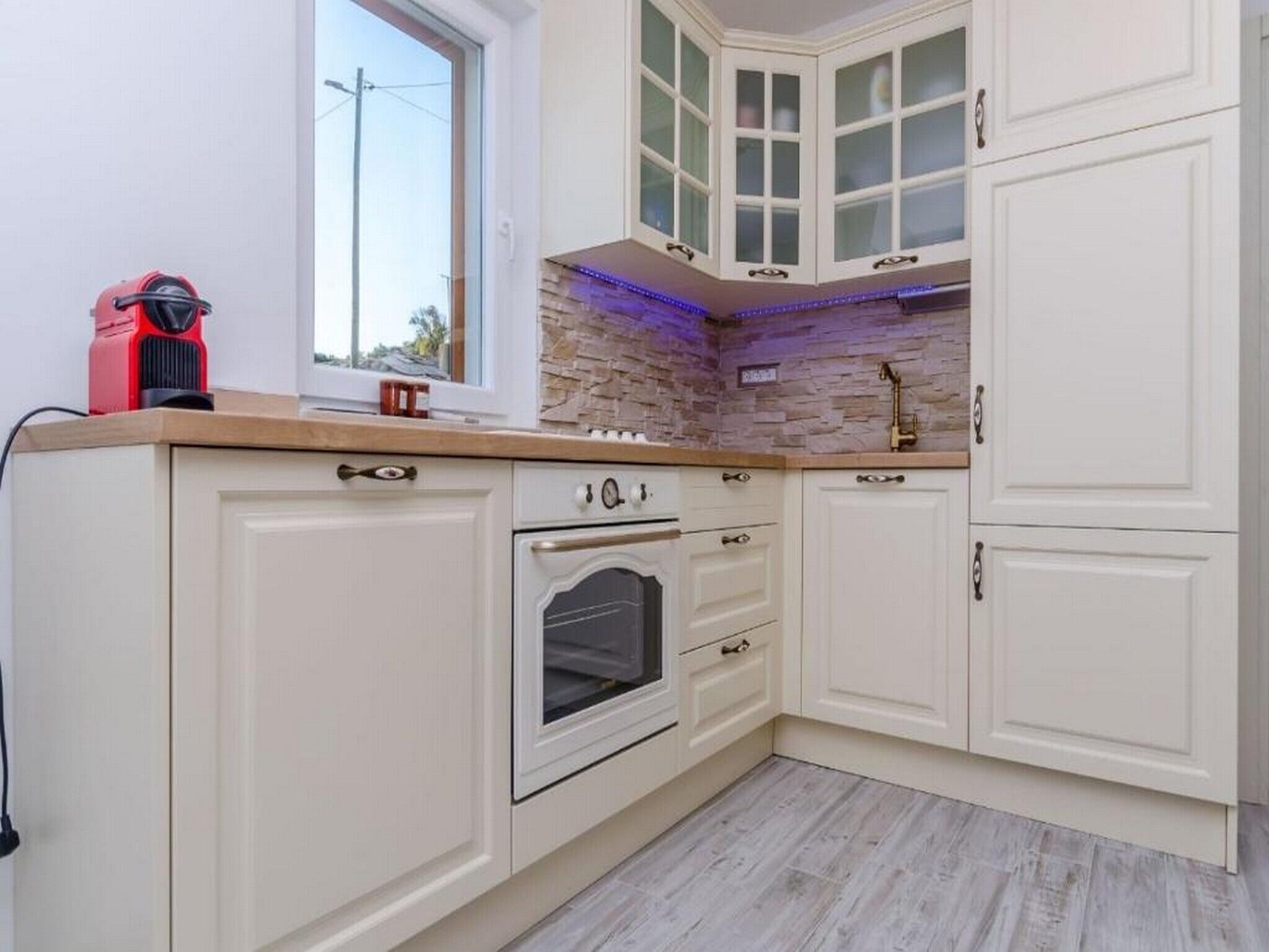 Una cocina con armarios blancos, horno empotrado y ventana con vistas.