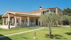 Une villa de style méditerranéen dotée d’un patio couvert, d’un espace salon extérieur et d’une pelouse bien entretenue.