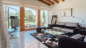 Un salon moderne avec une table basse en verre, des canapés sombres et un téléviseur à écran plat posé sur un meuble en verre.
