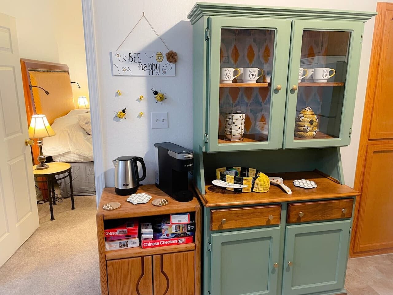 A kitchen with a green cabinet containing mugs and a coffee maker on the counter.