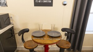 A small dining area with a round table, two chairs, and a red stool. There is a sign on the wall and a power outlet on the wall.