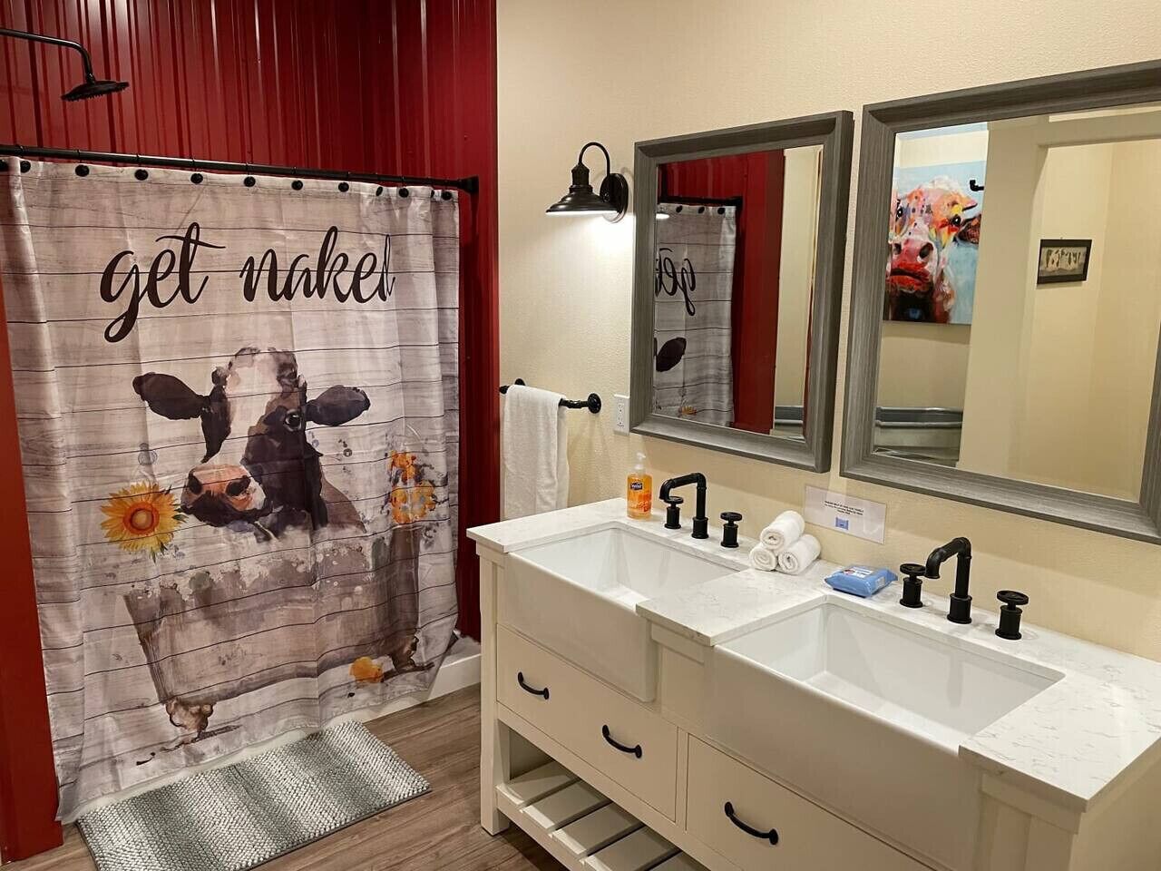 Une salle de bain équipée d’un lavabo double, d’un miroir, d’un porte-serviettes et d’un rideau de douche orné de motifs représentant une vache et des tournesols.