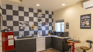A compact kitchen with a checkered backsplash, a red refrigerator, a coffee maker, and a small bar area with stools.