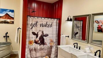 A bathroom with a large mirror, a bathtub, and a shower curtain with a cow and flowers design.