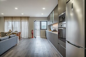 A modern kitchen with stainless steel appliances, a grey sofa, and a dining area with a table and chairs.