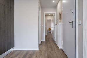 A hallway with a wooden floor, white walls, and a door with a mirror.