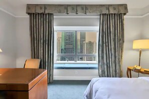 Ein Hotelzimmer mit Bett, Schreibtisch, Stuhl, Lampe und einem Fenster mit Vorhängen.
