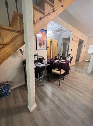 Un coin repas avec un escalier en bois, une table entourée de chaises et un tableau encadré accroché au mur.