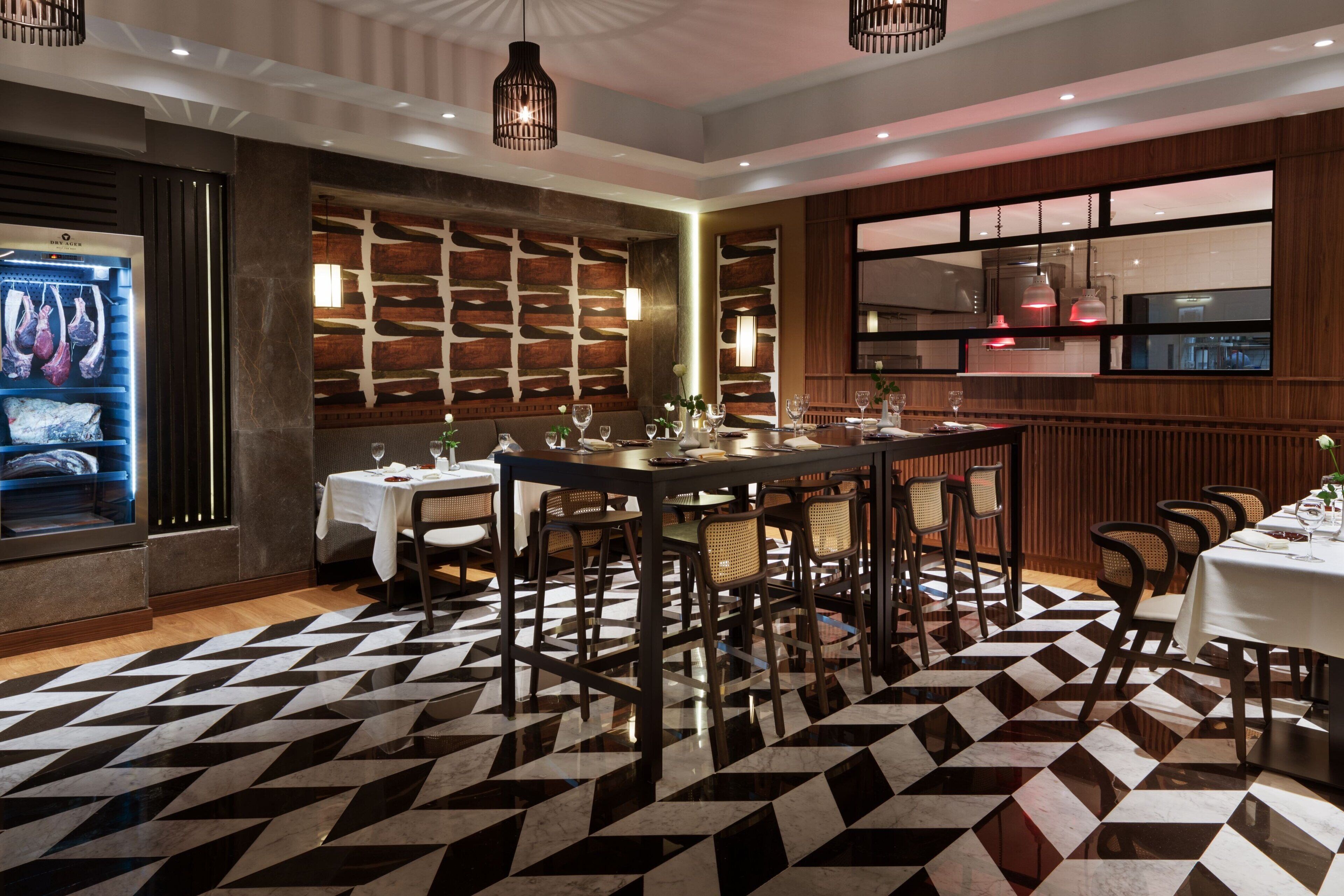 Un restaurante con suelo de diseño geométrico, paredes de paneles de madera y una lámpara moderna.