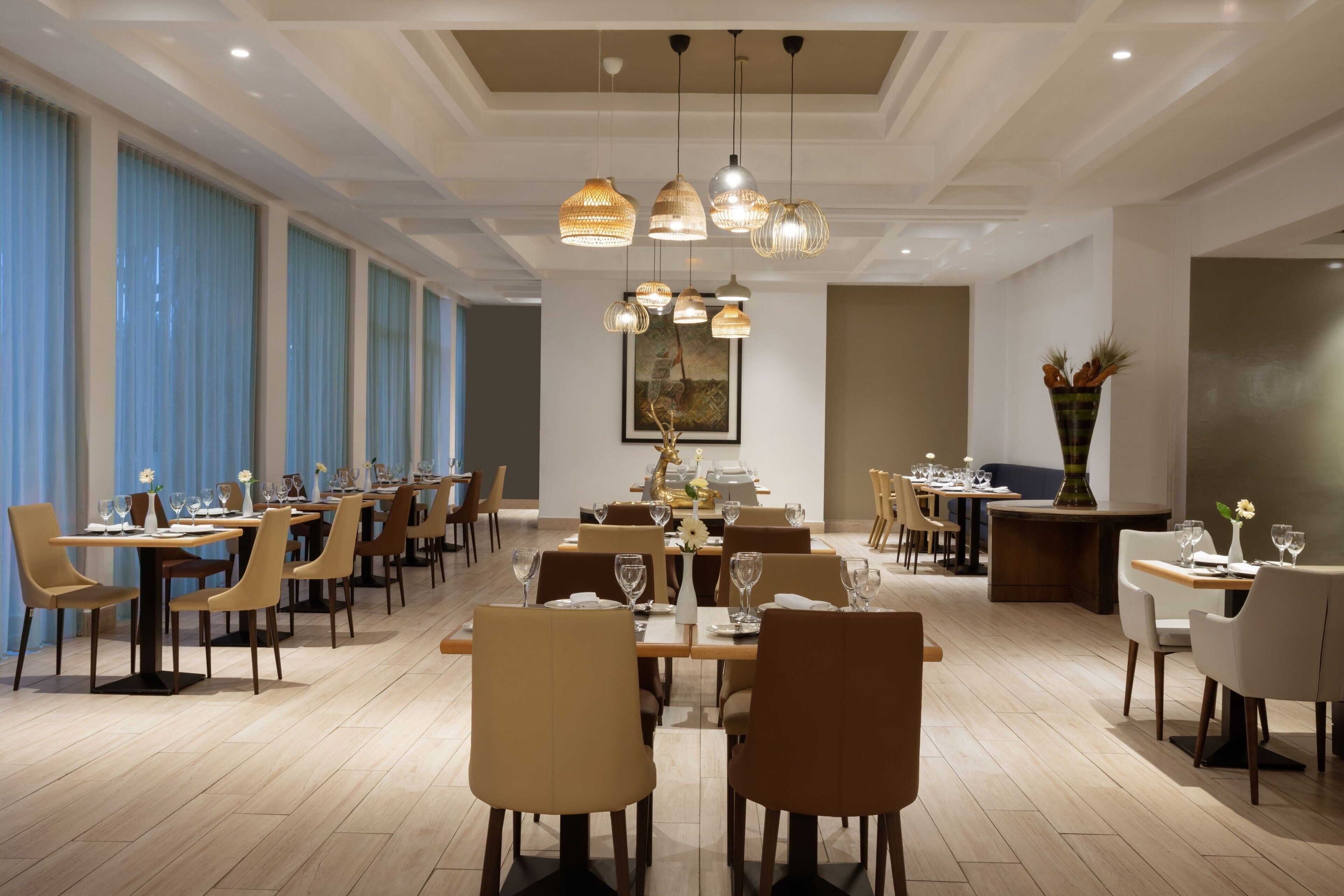 A spacious dining area with multiple tables and chairs, a central chandelier, and a painting on the wall.