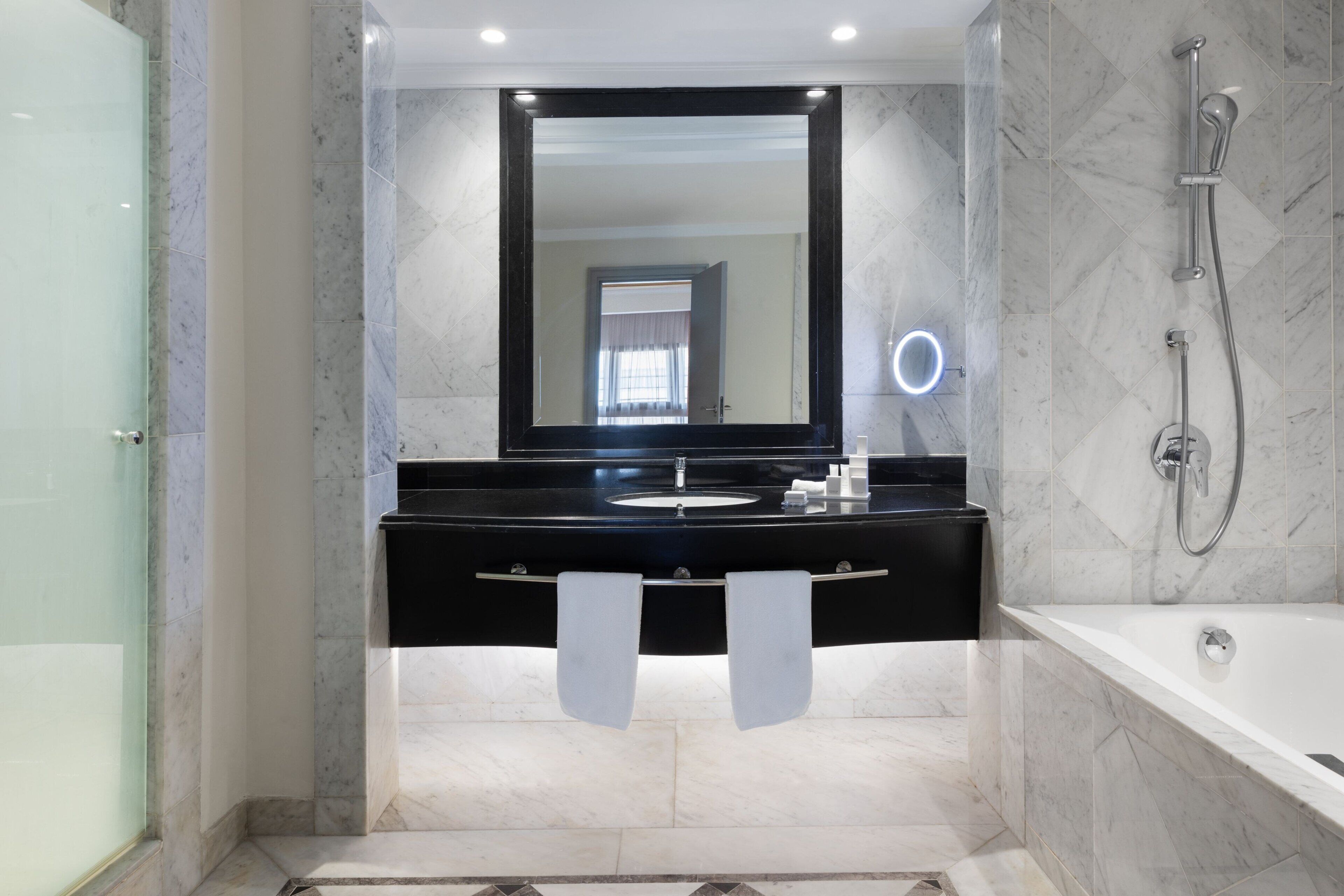 A modern bathroom with a black vanity, a large mirror, a handheld showerhead, and a bathtub.
