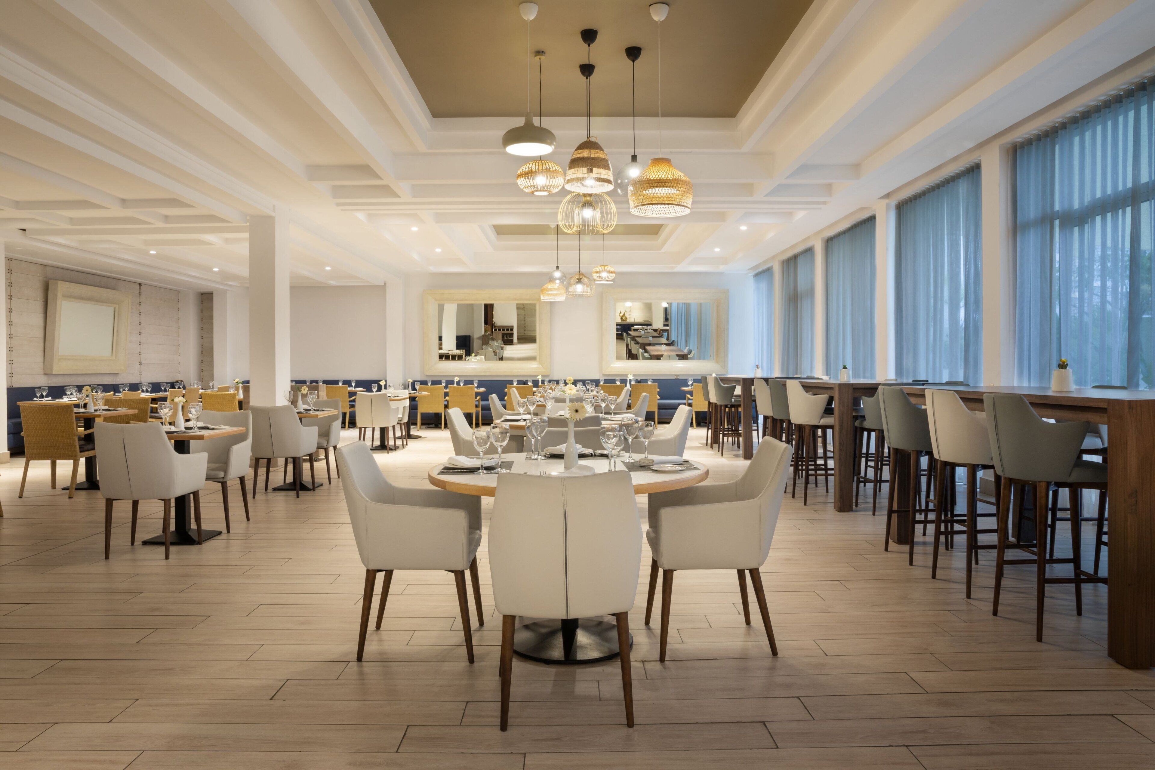 Un vaste espace dédié à la salle à manger, avec de nombreuses tables et chaises, de grandes fenêtres et des luminaires suspendus.