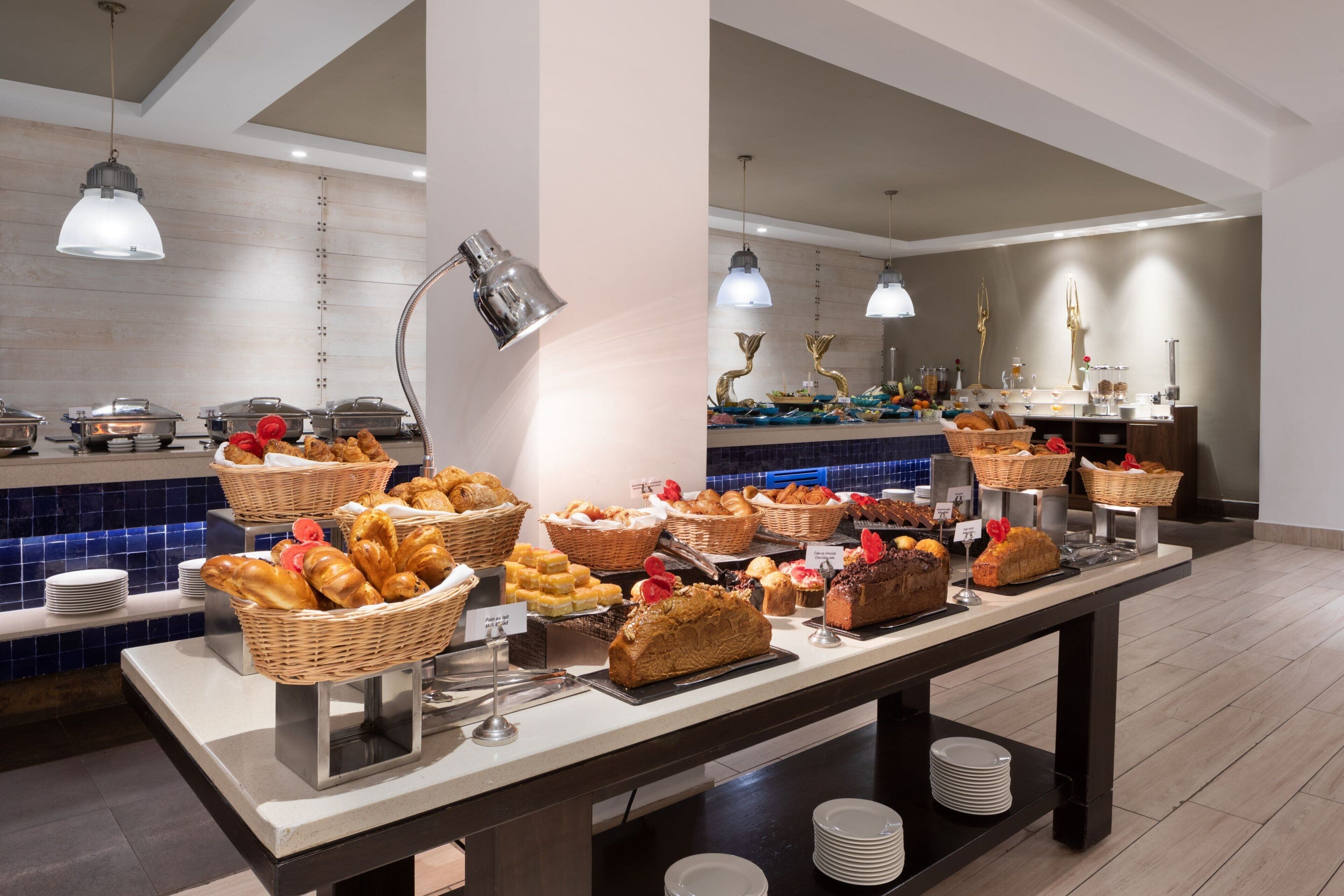 A buffet with various food items and baskets, a tiled backsplash, and hanging pendant lights.