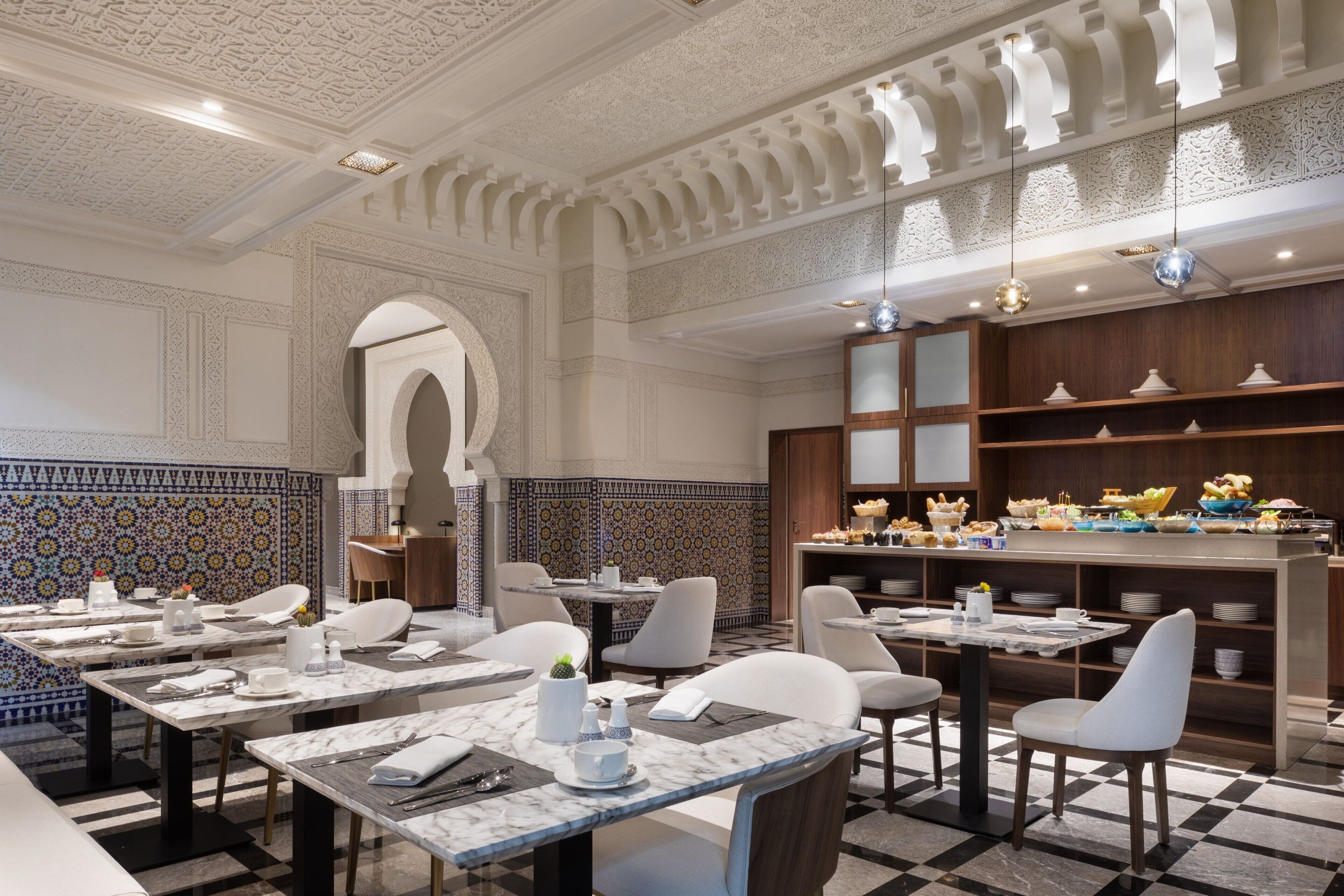 Un restaurante con mesas de mármol, sillas blancas y una pared de azulejos con diseño.