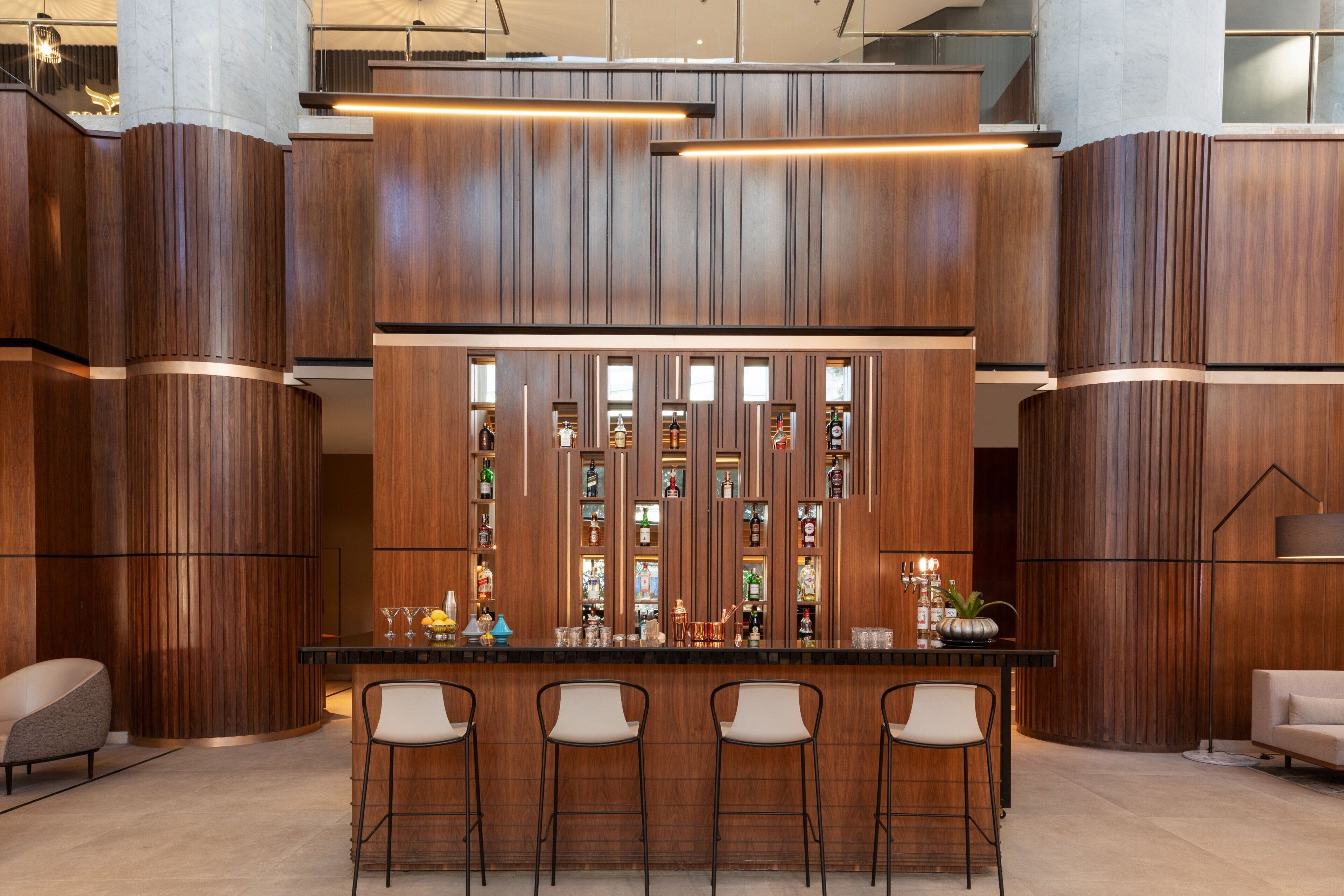 A bar area with a wooden panel design, bar stools, and a variety of bottles and glasses on the shelves.