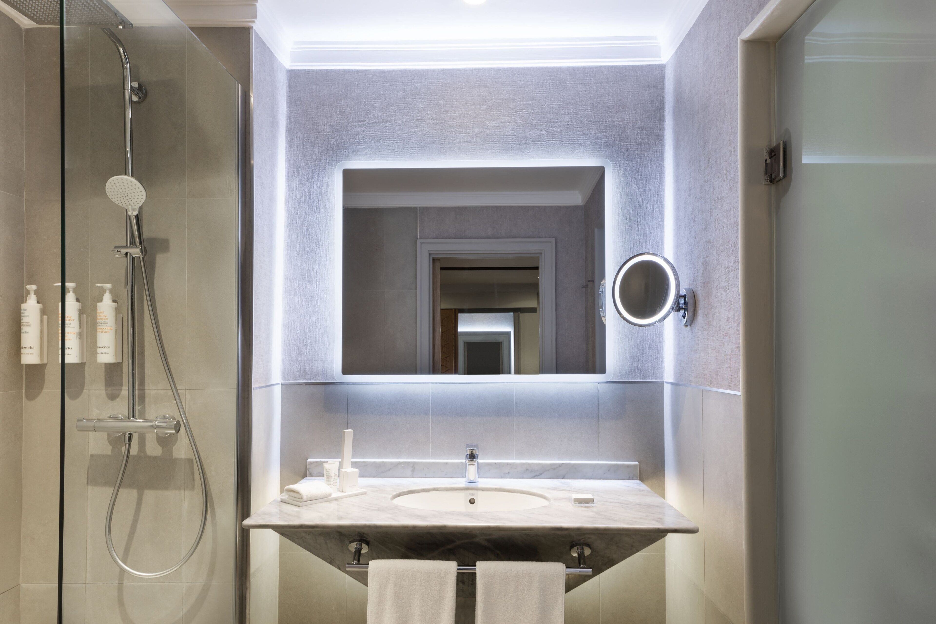 Un baño moderno con ducha envuelta en vidrio, un espejo grande y un lavamanos de mármol.