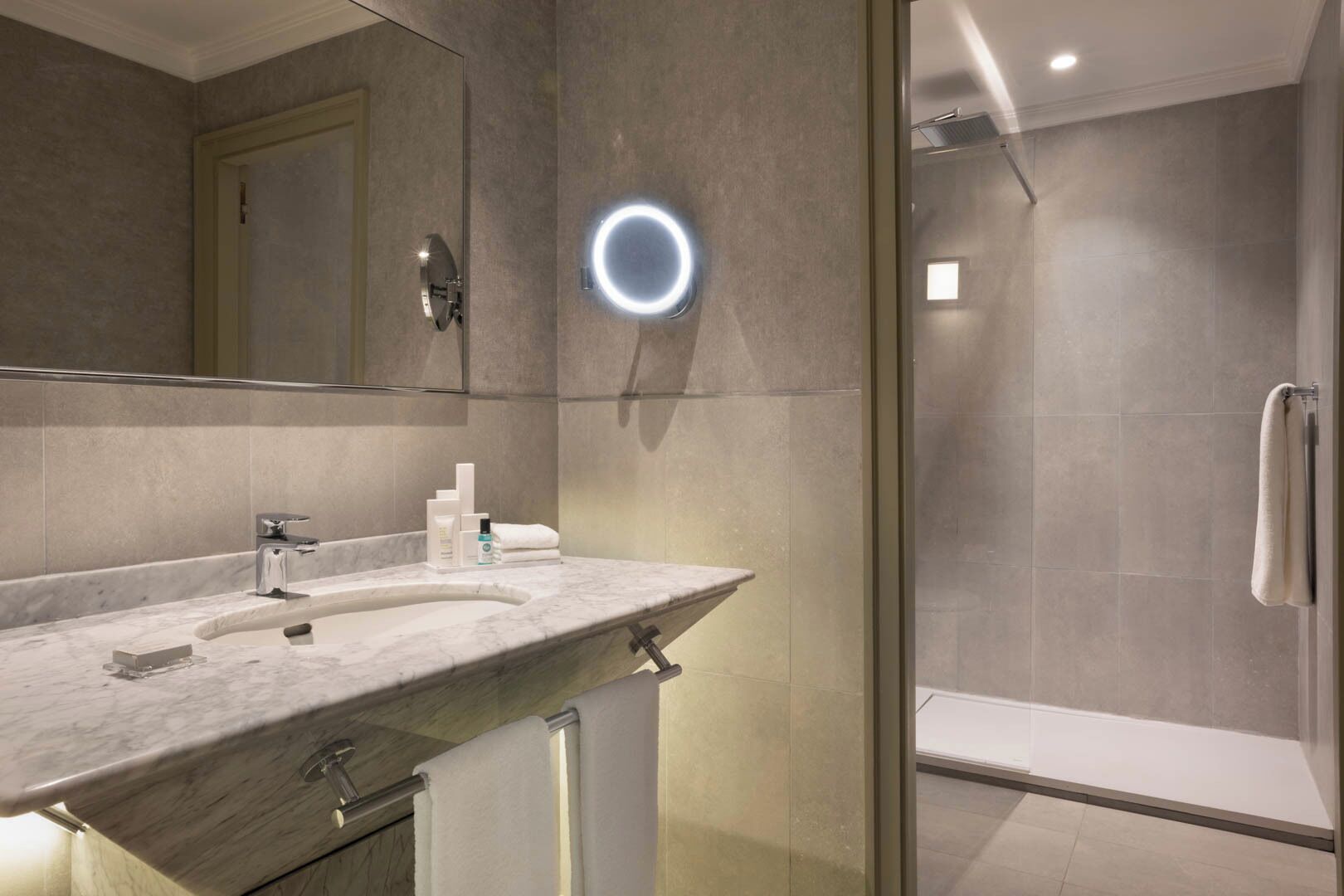 A modern bathroom with a marble sink, a large mirror, and a glass-enclosed shower.