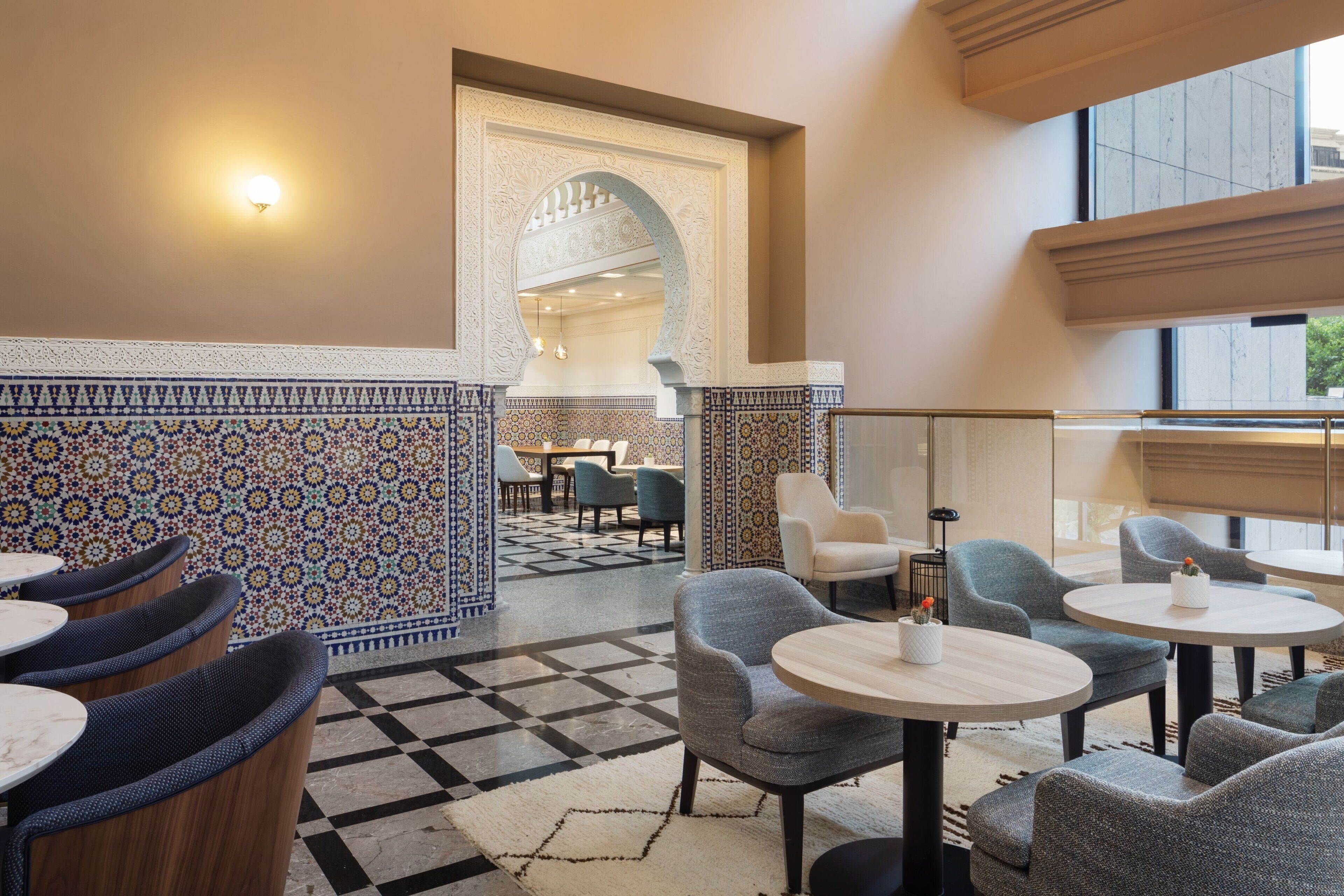 Un hall d’entrée avec des murs recouverts de carreaux décoratifs, un sol à motifs géométriques et des tables rondes entourées de chaises.