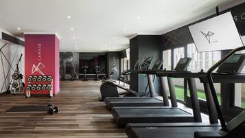 Un gimnasio con cintas de correr, mancuernas y un rack de pesas fijado a la pared.