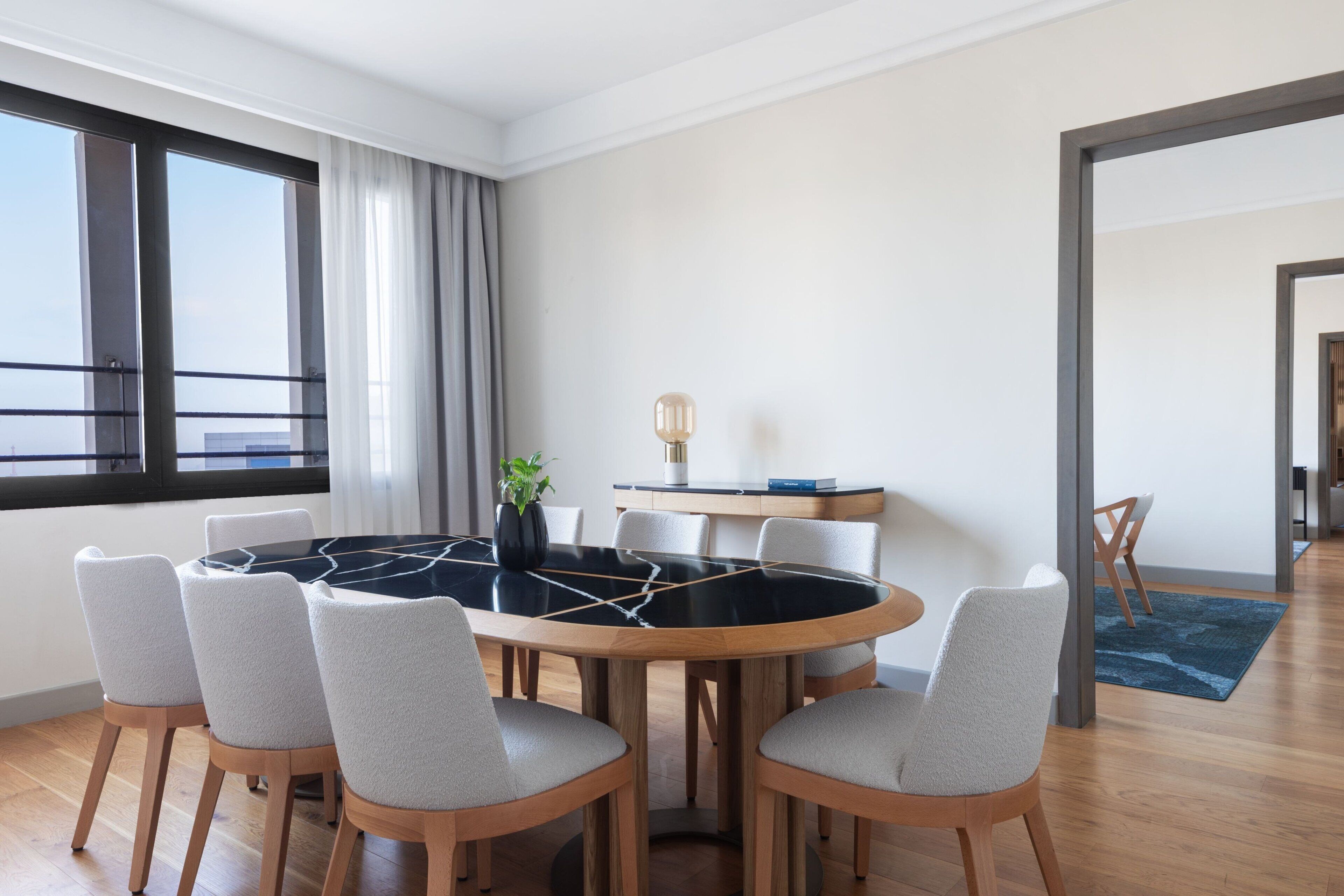 A modern dining area with a round table, six chairs, and a vase with a plant.