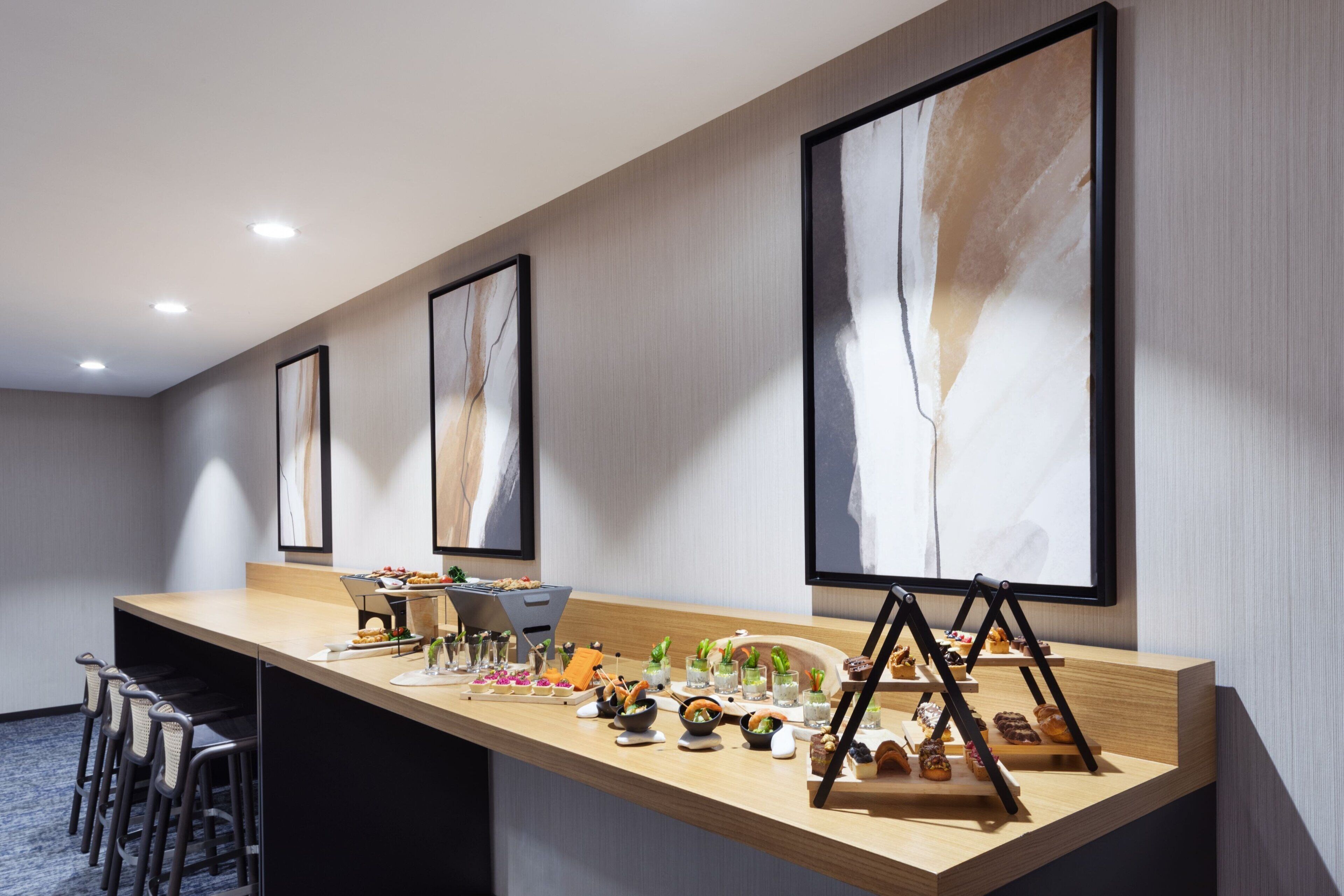 Un long comptoir d’accueil avec un revêtement en bois, agrémenté de tableaux abstraits encadrés, et un espace bar avec des tabourets.