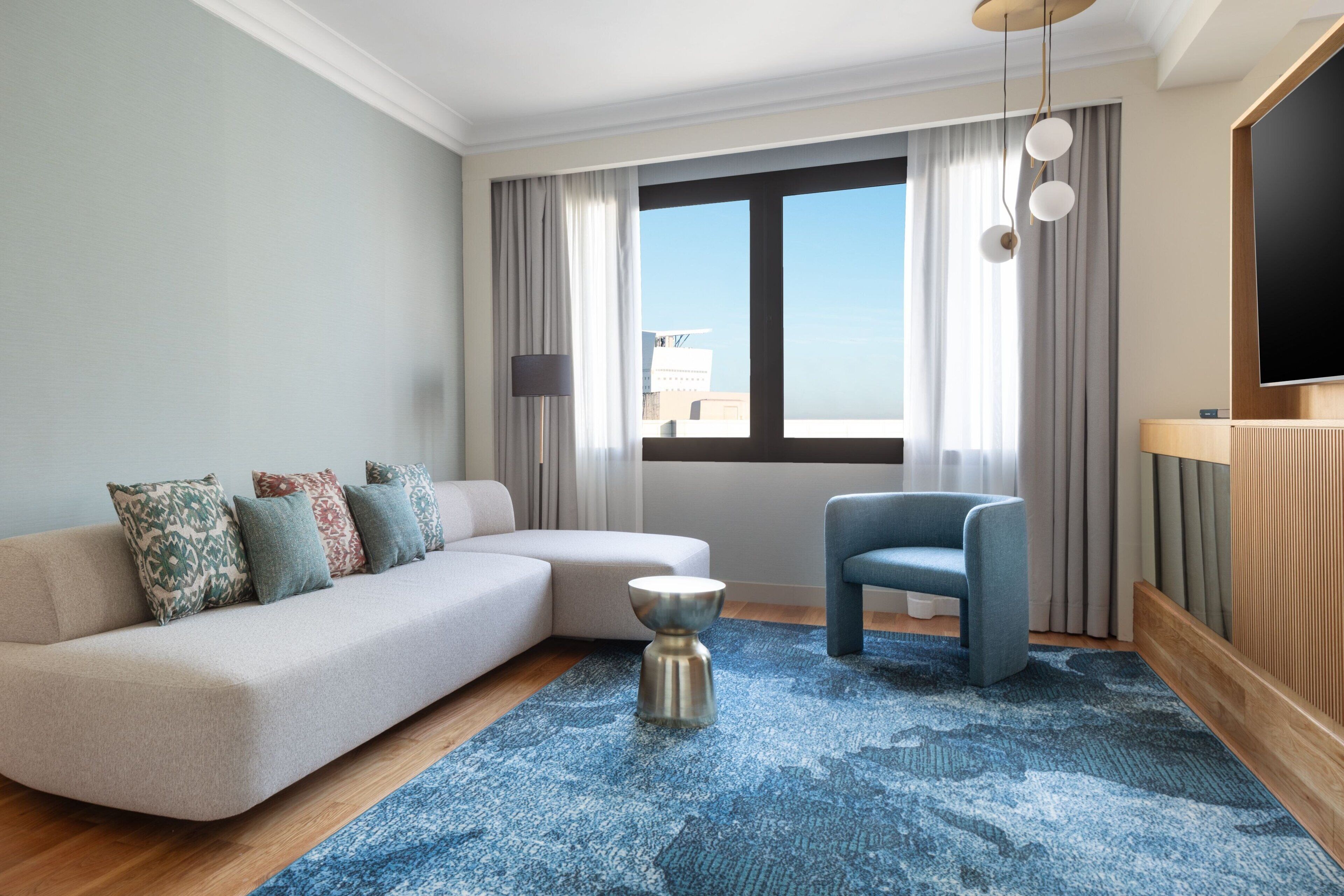 Una sala moderna con un sofá, un sillón, una mesa de centro y un gran ventanal con cortinas.