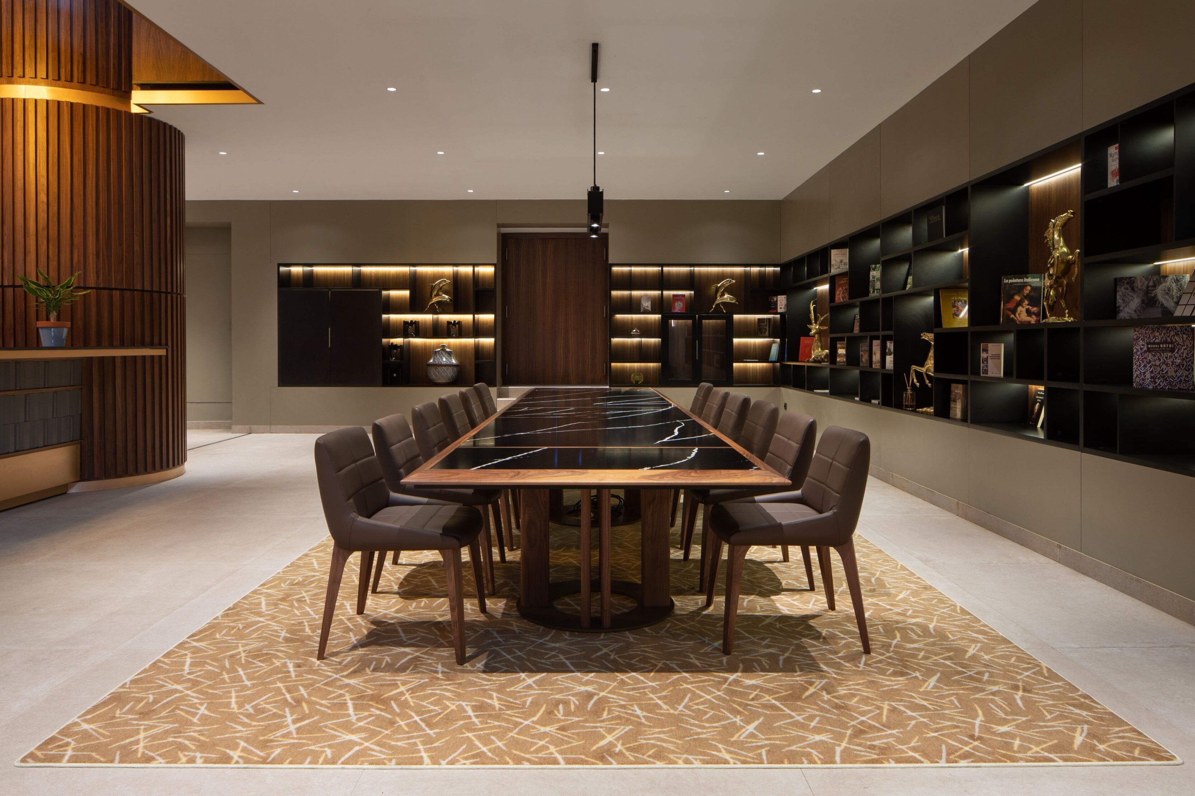 A modern dining area with a long table, chairs, and a patterned rug.