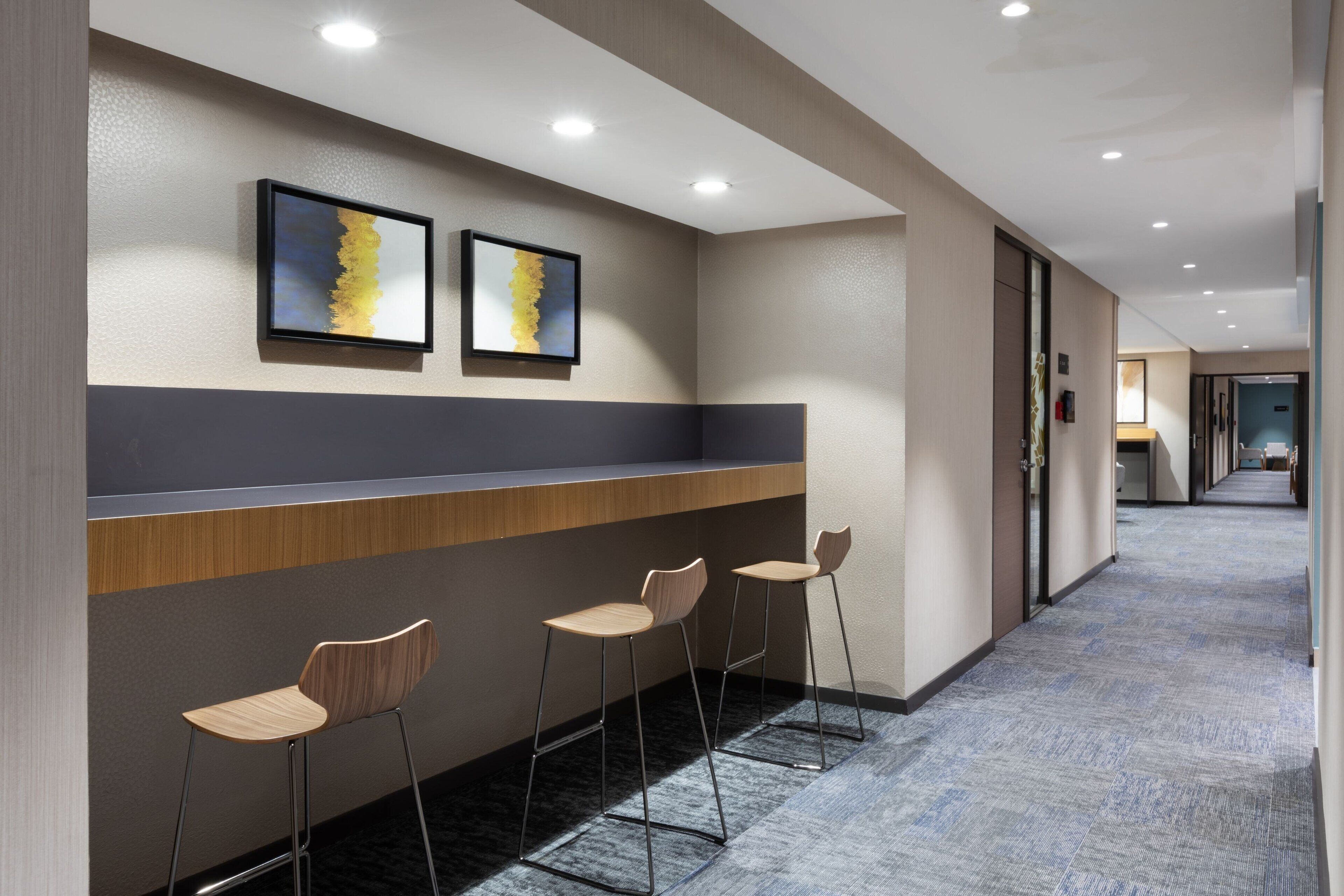 A modern hallway with a reception desk, two framed artworks, and three bar stools.
