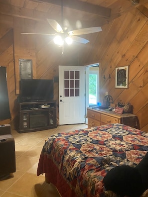 Una stanza accogliente con un letto, una televisione, una ventola a soffitto e una porta che dà sull'esterno.