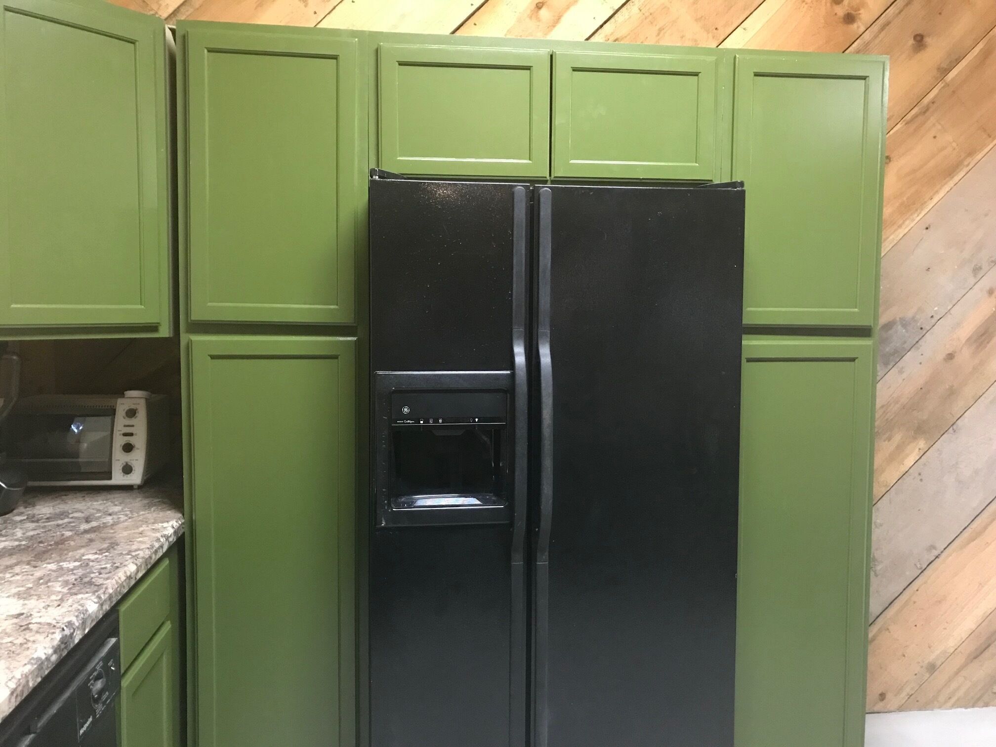 A kitchen with green cabinets, a black refrigerator, and a microwave.