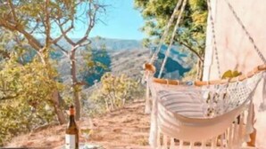 Una hamaca y una botella de vino en un patio de piedra con vistas a árboles y colinas.
